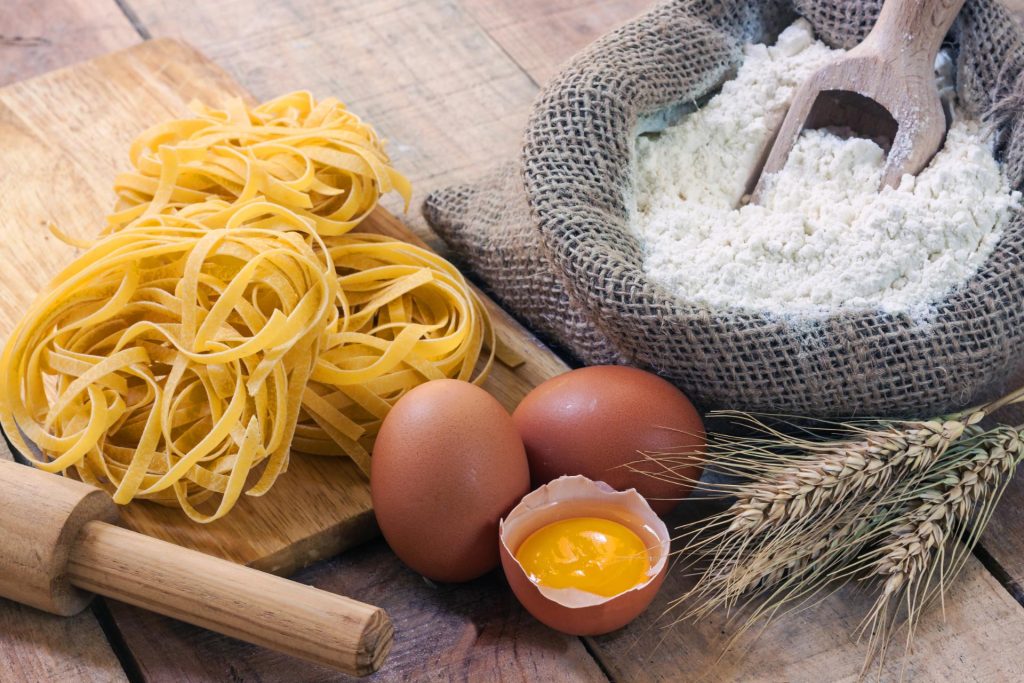Pasta italiana al lado de huevos, harina de maíz y un rodillo